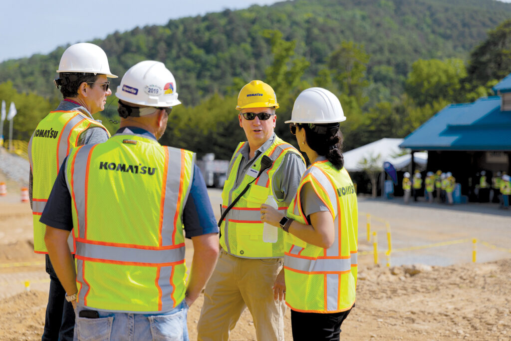 A group of four people, including three men and one woman, all wearing Komatsu hard hats and reflective vests. This is highlighting that it is important to speak up to stay safe.