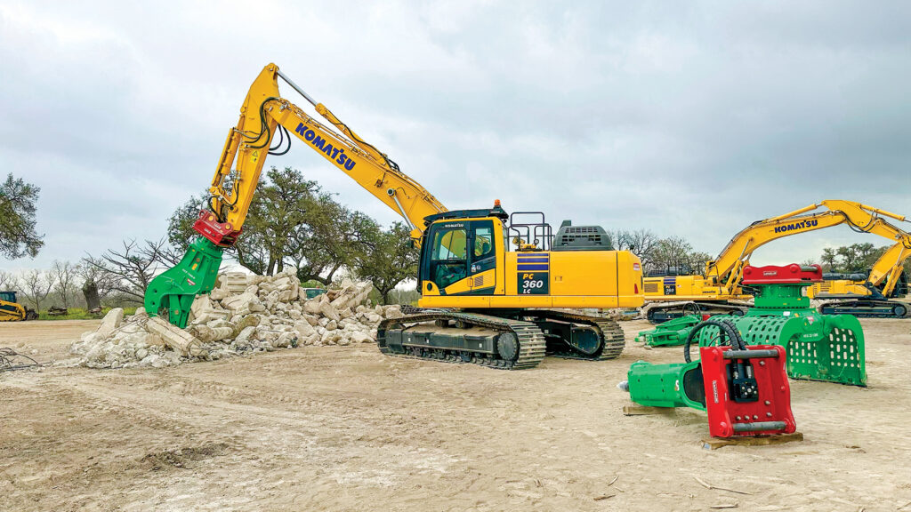 An attendee operates a Komatsu PC360LC-11 excavator with a straight boom equipped with a Lehnhoff SQ80V fully automatic symmetric quick coupler and a Montabert HCP 1000-R pulverizer. Other attachments surround the excavator.
