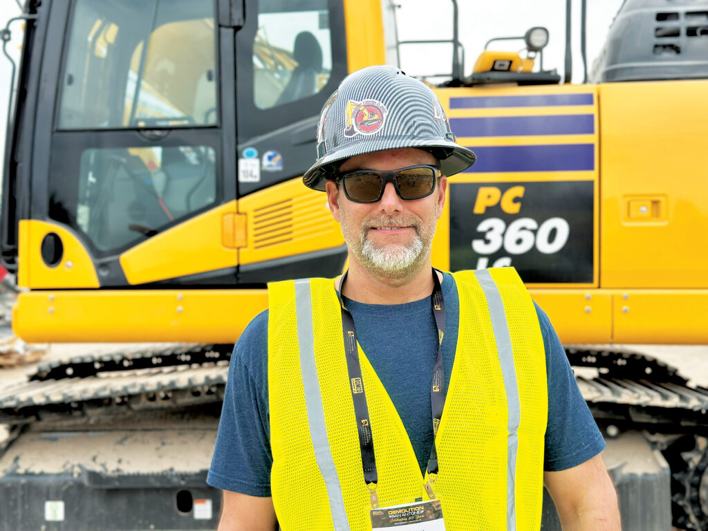 An image of Rodney Loftis, President of Rodney Loftis & Son Contracting, wearing a hard hat and reflective vest, standing in front of a Komatsu PC360LC Excavator.